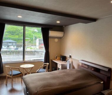 Western-style guest room with beds and riverside window at Ryokan Tenryu in Ōita