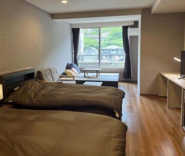 Bright twin room with wooden floors, sofa seating and balcony at Ryokan Tenryu in Ōita