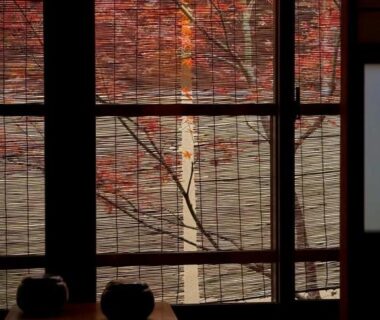 View through bamboo blind showing red maple leaves outside and a low wooden table inside at Ryokan Tori Kyoto
