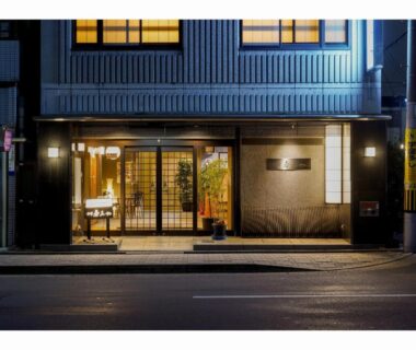 Nighttime lit entrance with wooden-framed glass doors and small lobby, Ryokan Wakamiya in Kyoto