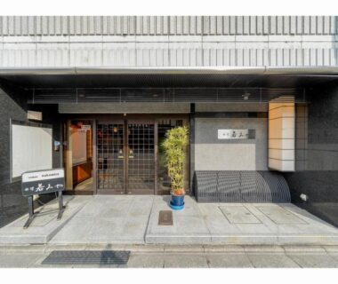 Entrance facade with wooden lattice door and potted plant at Ryokan Wakamiya in Kyoto