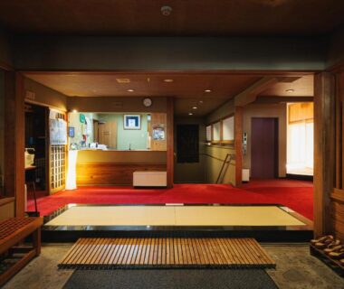 Genkan entrance with red carpet, slippers and reception desk at Ryokan Warabino in Nagano, Chūbu