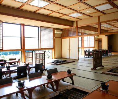 Spacious tatami dining area with low wooden tables, shoji screens and floor seating at Ryokan Warabino in Nagano