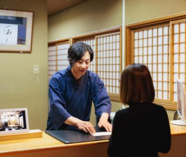 Staff in traditional attire assisting guest at wooden reception with shoji screens at Ryokan Warabino in Nagano