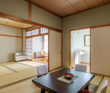 Tatami room with low wooden table, shoji screens, zabuton cushions and adjoining washbasin area at Ryokan Warabino, Nagano