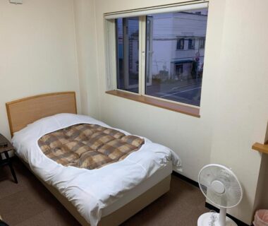 Single bed with patterned duvet and window in Ryokan Yamaichi guest room Hokkaidō