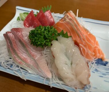 Assorted sashimi slices including salmon, tuna, and prawn on shredded daikon with parsley garnish on ceramic plate