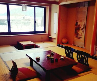 Traditional tatami room with low wooden table, floor cushions and tokonoma at Ryokan Yamakanoyu in Nagano