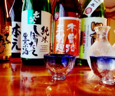 Sake bottles with glass carafe and cups on wooden counter at Ryokan Yamakanoyu, Nagano