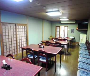 Communal dining area with wooden tables, chairs, shoji screens and seating cushions at Ryokan Yamamuro in Ishikawa