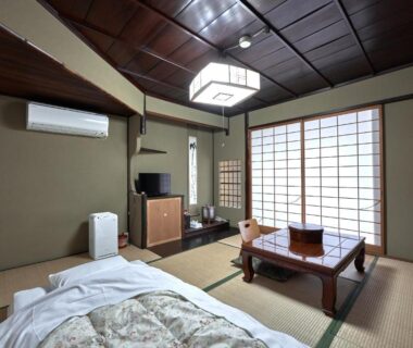 Traditional tatami room with futon bedding, low wooden table, shoji screens and TV at Ryokan Yamamuro in Ishikawa