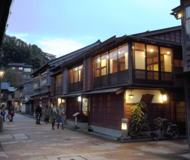Evening street of wooden ryokan facades with lit shoji windows at Ryokan Yamamuro in Ishikawa, Chūbu