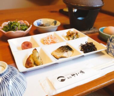 Compartment tray with grilled fish, pickles, seaweed and small bowls on wooden table at Ryokan Yamanoyu Kumamoto