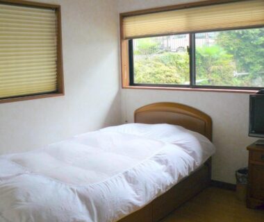 Single bed room with wooden headboard, white duvet and garden view at Ryokan Yamashiroya in Ōita, Kyushu