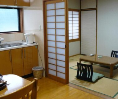 Tatami seating area with low table, shoji screens and small kitchenette at Ryokan Yamashiroya Oita