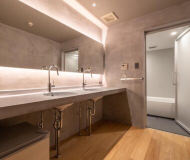 Double sink vanity with large mirror and wooden floor leading to a bathtub alcove in minimalist washroom