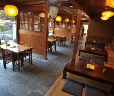 Indoor ryokan dining with low tables, tatami seating, wooden partitions and lanterns overlooking a small garden in Kyoto