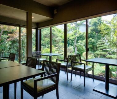 Dining area with wooden chairs and tables, floor-to-ceiling windows overlooking lush garden at Ryokan Yoshidaya, Saga