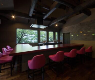 Long wooden table with pink chairs facing windows and lush garden at Ryokan Yoshidaya in Saga