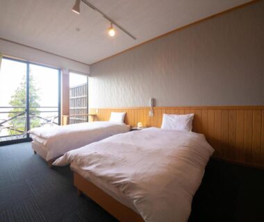 Twin Western beds with wooden headboard and sliding glass doors opening to balcony with treed view