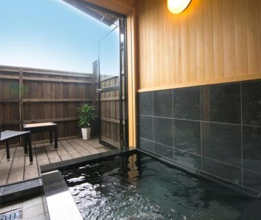 Indoor tiled onsen bath opening to a small wooden terrace with chairs at Ryokan Yufusan, Oita