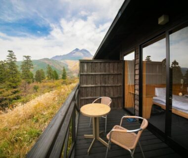 Wooden balcony with table and chairs overlooking mountain and pine trees at Ryokan Yufusan in Ōita, Kyūshū, Japan