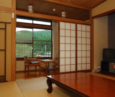 Traditional tatami room with low table, shoji screens and window seating overlooking garden at Ryokan Yunosako, Kumamoto