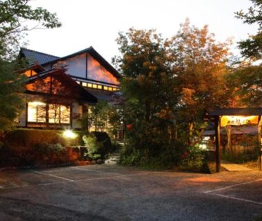 Twilight-lit ryokan entrance framed by trees with warm interior lighting at Ryokan Yunosako, Kumamoto