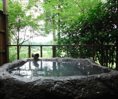 Stone outdoor bath framed by wooden screens, overlooking lush greenery at Ryokan Yunosako in Kumamoto