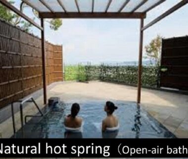 Two guests soaking in an outdoor onsen under a wooden pergola with bamboo screening and greenery