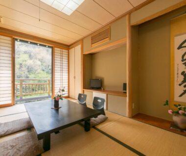 Traditional tatami room with low table, shoji screens, calligraphy scroll and balcony overlooking wooded hillside in Gifu
