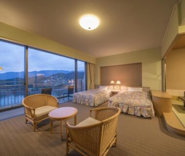Spacious twin room with tatami seating and large windows overlooking water and distant town at Ryoso Uminocho