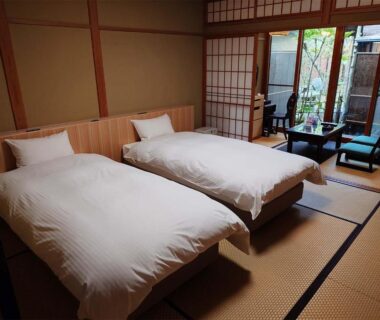 Tatami room with twin Western beds, shoji screens and low seating overlooking courtyard garden at Ryoso Yufuin Yamadaya, Ōita