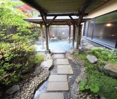 Stone path to outdoor onsen with wooden pergola at Ryotei Hanayura in Hokkaidō surrounded by moss and shrubs