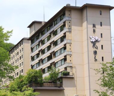 Multi-story ryokan building with balconies surrounded by green trees in Hokkaidō