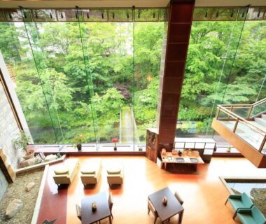 Spacious lobby seating with floor-to-ceiling glass facing lush forest at Ryotei Hanayura Hokkaidō, Japan