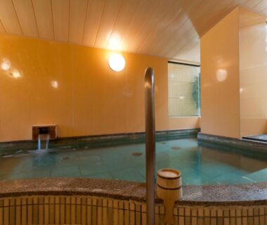 Indoor onsen pool with wooden ceiling, tiled edge, handrail and bench seating at Ryotei Manyou, Ishikawa