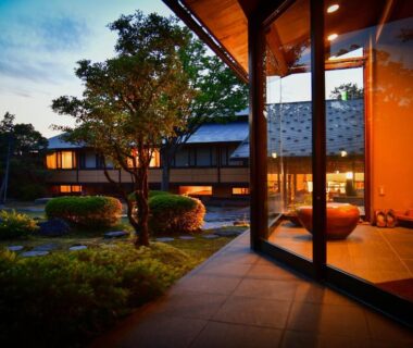 Lit entrance corridor with glass doors overlooking a landscaped Japanese garden at Ryotei Manyou in Ishikawa
