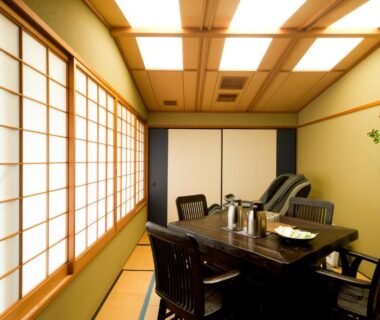 Tatami room with dining table, shoji screens, chairs and tokonoma flower alcove at Ryotei Manyou in Ishikawa, Japan