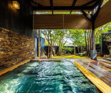 Wooden onsen bath with stone wall and decking opening to a serene garden at Ryotei Matsubaya, Oita