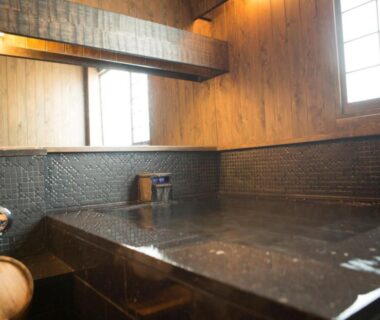 Indoor wooden bath with stone edge and shoji window at Ryotei Matsuya Honkan Suizenji