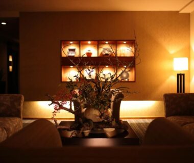Dimly lit ryokan lounge with sofas, illuminated display shelves, central floral arrangement and shoji screen window