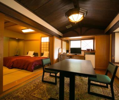 Tatami room with low table, western bed, shoji screens and wooden ceiling at Ryotei Tanokura, Ōita