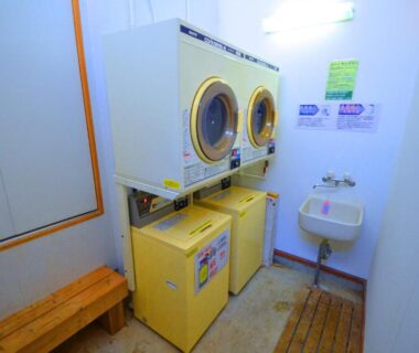 Stacked washer and dryer with wooden bench and small sink in Ryoufuso laundry room, Mie