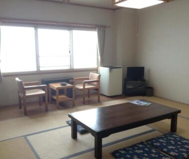 Simple tatami room with low table, chairs by window, small TV and compact refrigerator