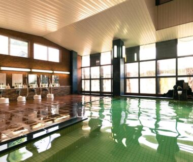 Large indoor onsen pool with tiled floor, row of washing stations and floor-to-ceiling windows at Ryounkaku Matsunoyama, Niigata
