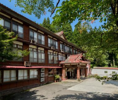 Three-story wooden ryokan facade with traditional windows and entrance amid verdant trees in Niigata