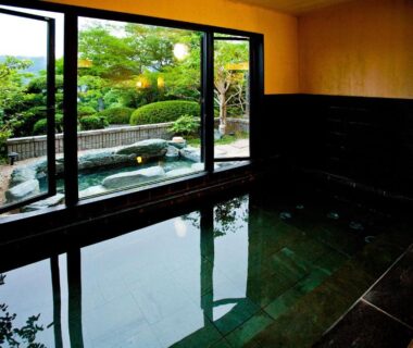 Stone-tiled indoor onsen with floor-to-ceiling windows overlooking garden and outdoor bath at Ryouri no yado Ginrin, Mie