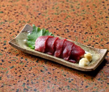 Thinly sliced red sashimi on ceramic plate with shiso leaf and grated ginger on patterned tabletop