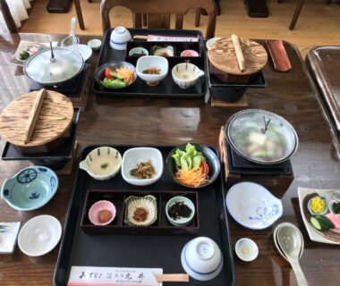 Wooden table laid with traditional Japanese meal set, small bowls, covered pots, condiments and chopsticks